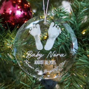 Clear glass round ornament engraved with baby footprints, name, and date