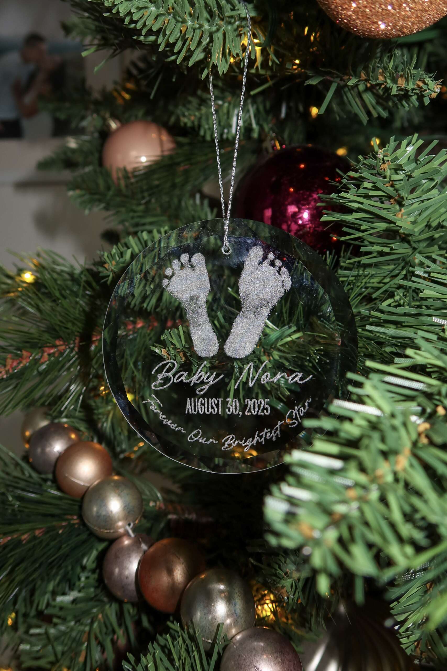 Clear round glass ornament engraved with baby footprints and personalized name