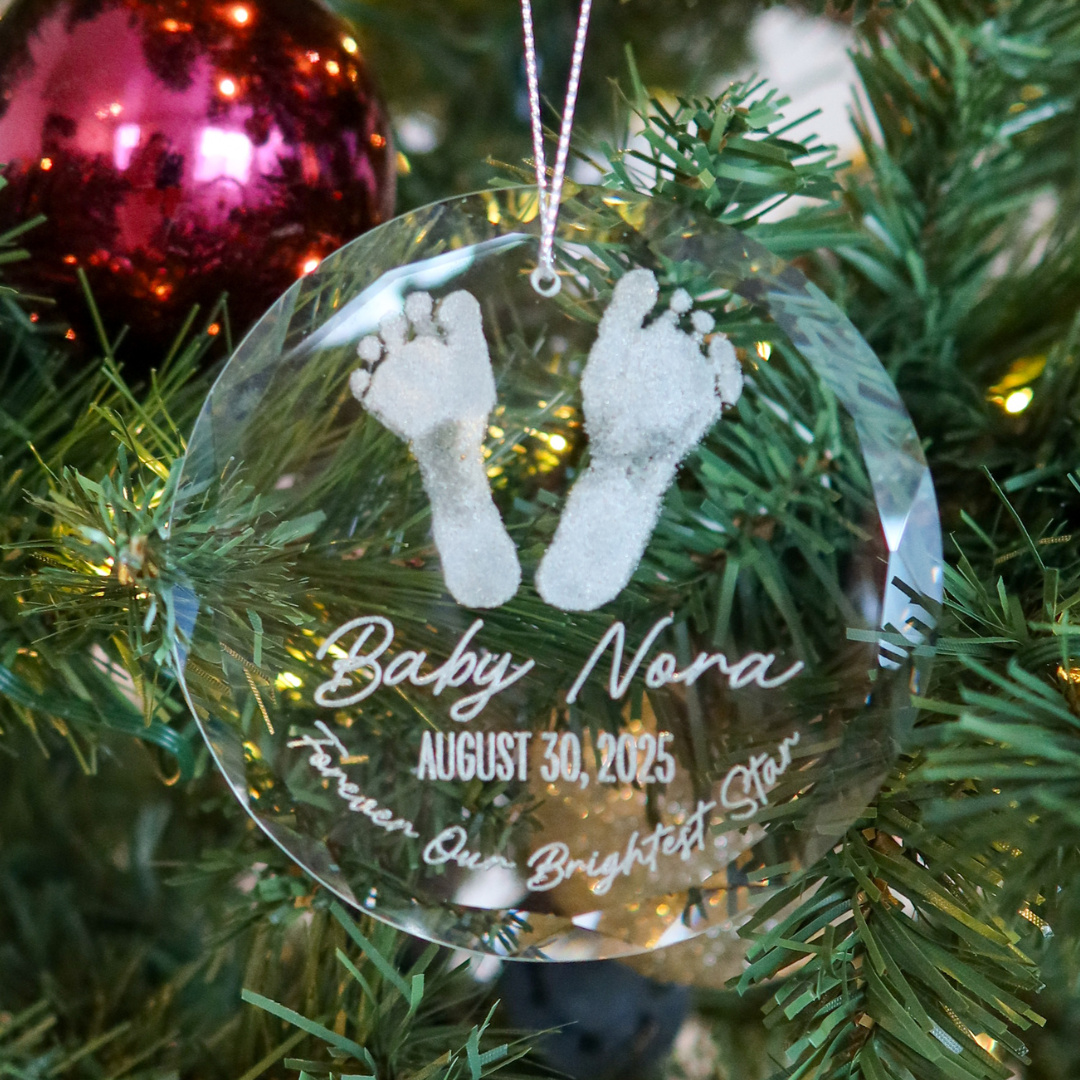 Clear glass round ornament engraved with baby footprints, name, and date